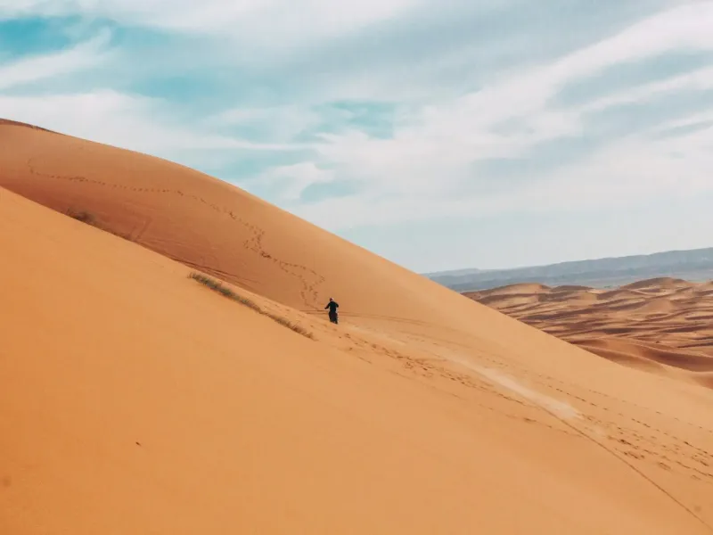A single figure walking the crest of a tall sand dune in the Sahara near Merzouga.