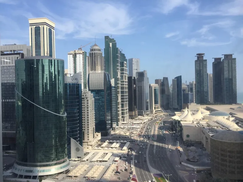 The West Bay towers of Doha seen from above, with the Corniche traffic and the sea beyond