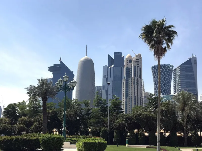 The West Bay skyline of Doha rising behind palm trees and parkland.