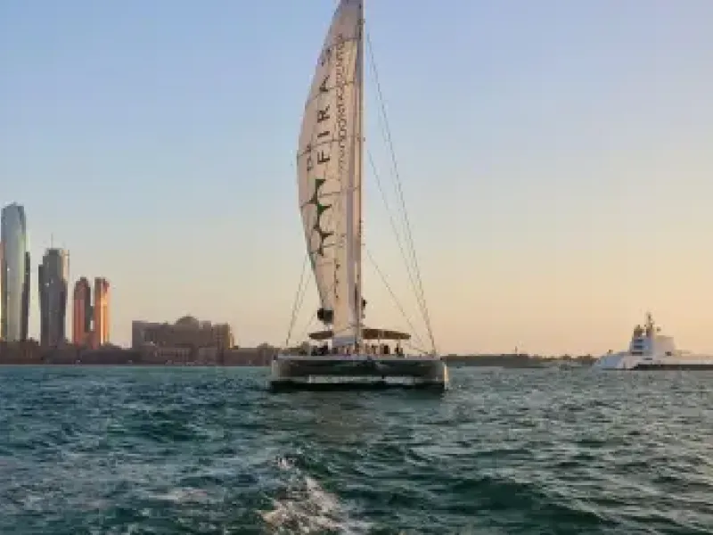 A sailing catamaran on the water off the Dubai coast at dusk.