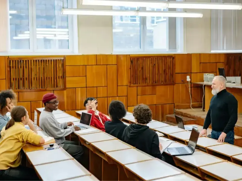 A classroom scene where a lecturer engages students seated with laptops in a modern lecture hall