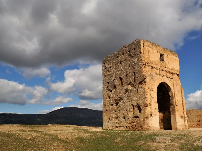 A weathered stone gateway standing alone on a green plain under a cloudy sky.