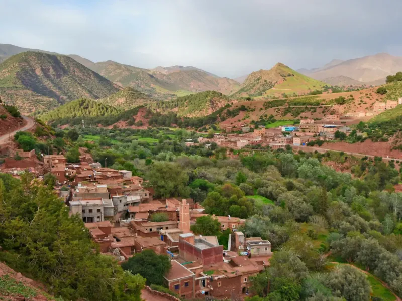 Red earth houses of a High Atlas village stepped above a green terraced valley.