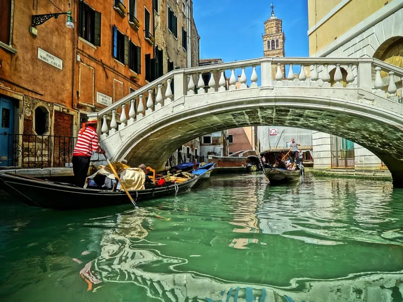 A gondolier steering under a stone bridge on a narrow Venetian canal