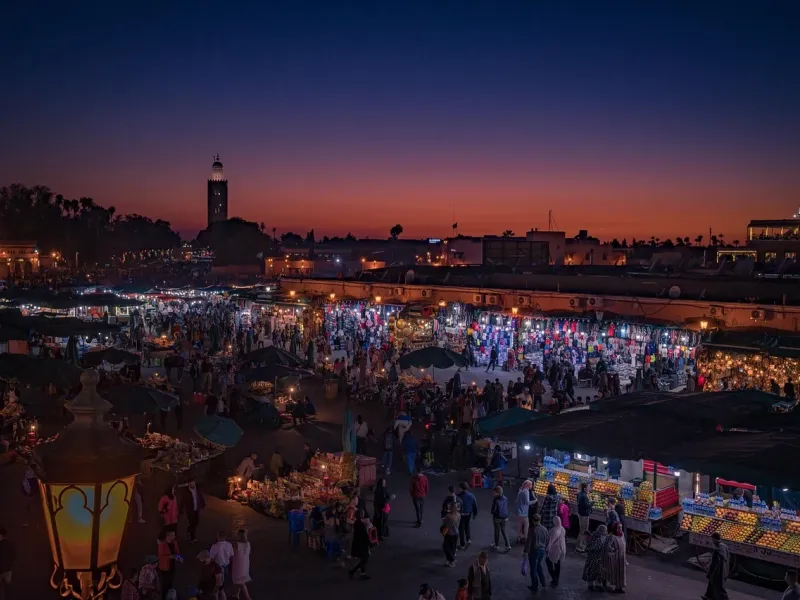 Food stalls and crowds filling Jemaa el-Fna square in Marrakesh at dusk, the Koutoubia minaret lit behind.