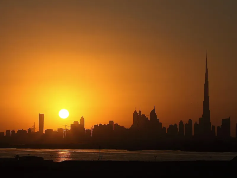 The Dubai skyline in silhouette against an orange sunset.