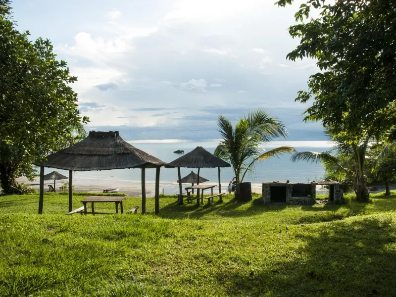 Thatched-roof huts and picnic tables on a grassy lawn by Lake Malawi featured