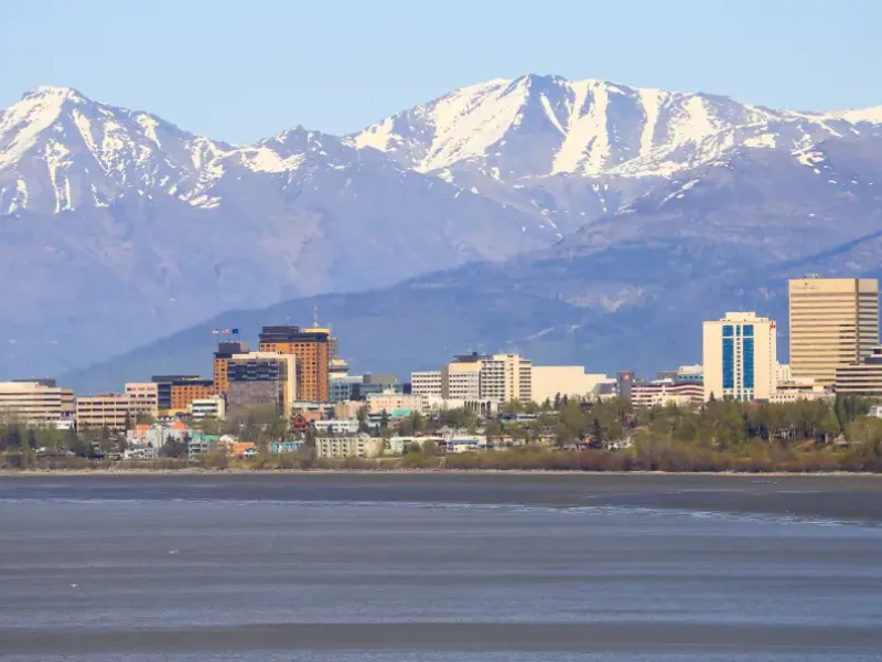 Anchorage; Alaska downtown skyline with snow-capped Chugach Mountains behind and Cook Inlet waters in foreground.