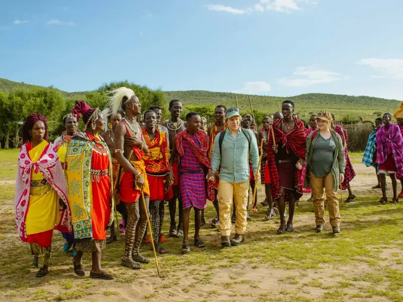 Two tourists walk with Maasai community members in traditional red attire during a cruise-land cultural village excursion