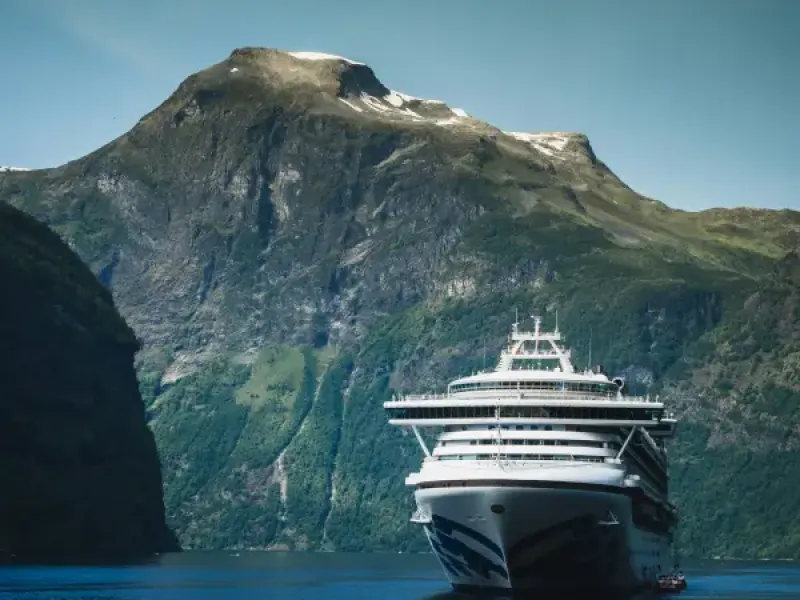 Princess Cruises ship sailing through a dramatic Norwegian fjord with steep green mountains and snow-capped peaks in the b