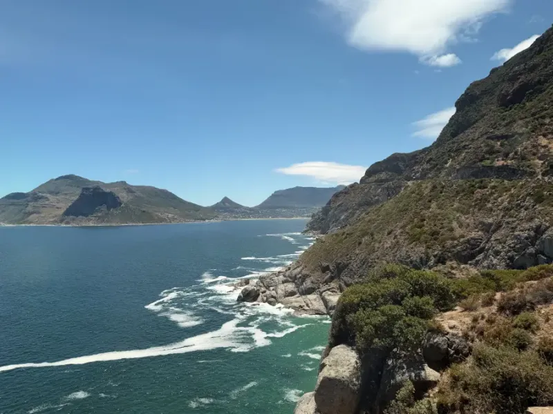 Dramatic rocky cliffs overlooking Hout Bay's turquoise waters with mountain backdrop; captured for eat-mea-2026 travel sho