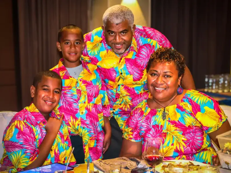 A smiling family of four wearing matching tropical print shirts enjoy a cruise dinner together at a festive table.
