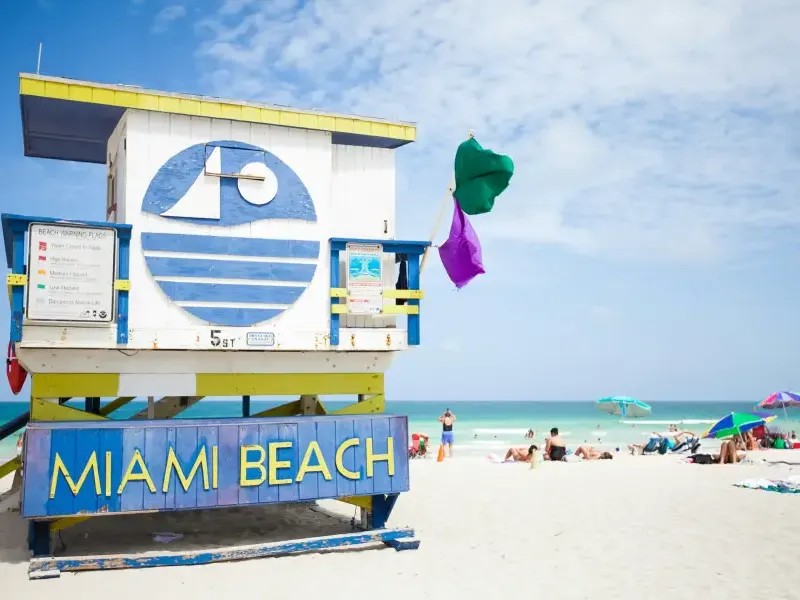 Colorful Miami Beach lifeguard station at 5th Street with green and purple warning flags flying on a sunny day.