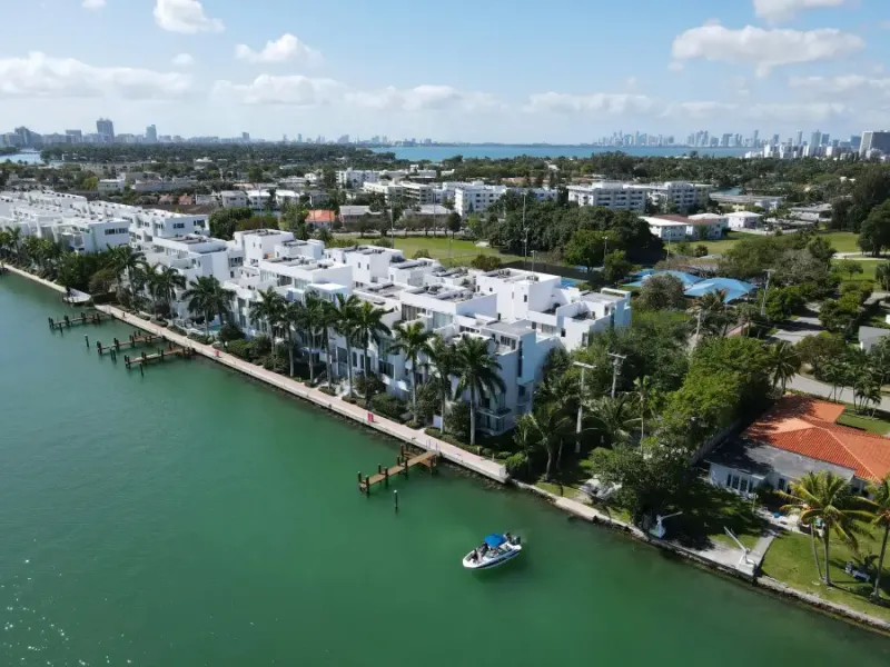Aerial view of white modern waterfront condos along Miami Florida's Biscayne Bay with downtown skyline in background.
