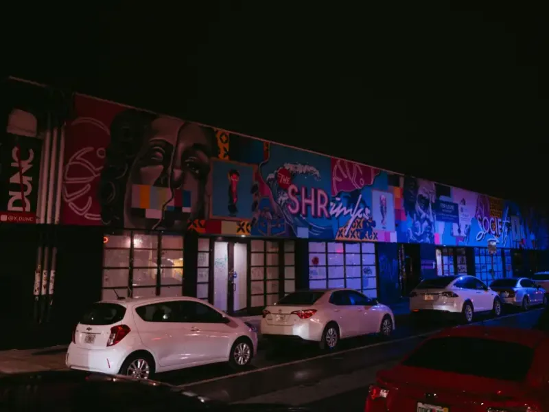 Colorful street murals illuminate a building facade at night in Miami; Florida's Wynwood arts district; with cars parked o