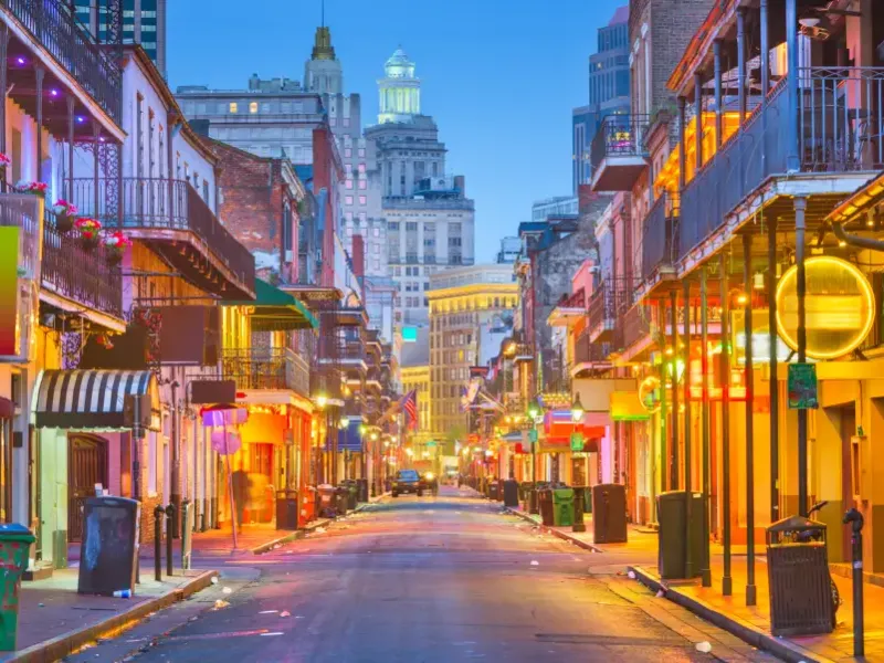 Bourbon Street in New Orleans Louisiana glows with colorful neon lights and iron-lace balconies at dusk with the city skyline beyond