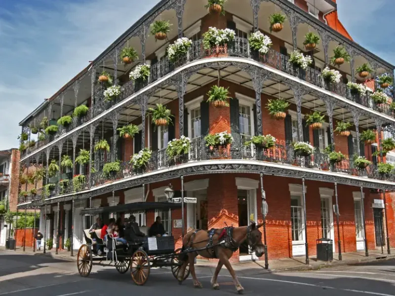 Horse-drawn carriage passes ornate iron-lace balconied brick building at Royal and Dumaine streets in New Orleans Louisiana
