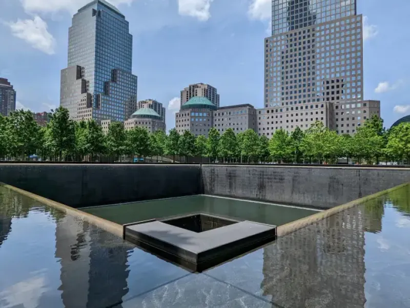 9/11 Memorial reflecting pool with cascading waterfall and Manhattan skyline in New York New York on a sunny day