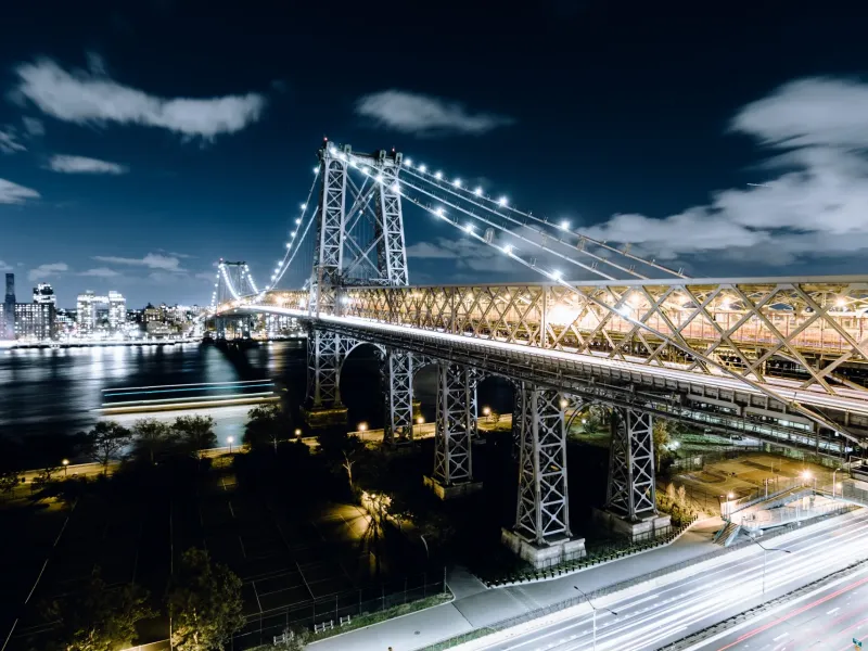 Williamsburg Bridge illuminated at night over the East River with the New York New York Manhattan skyline glowing in the background