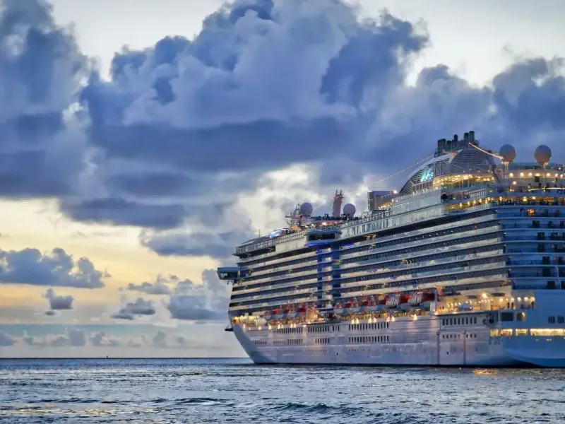 Regal Princess cruise ship illuminated at dusk; sailing calm ocean waters under dramatic cloudy sky.