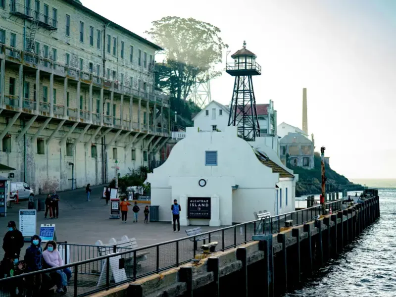 Visitors at Alcatraz Island dock in San Francisco; CA; with historic prison building and watch tower in background.