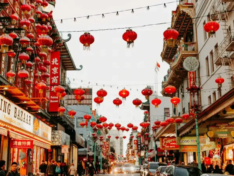 Red lanterns line Grant Avenue in San Francisco; CA's Chinatown; with shops and pedestrians along a vibrant street at dusk.