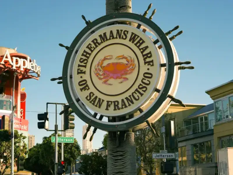 Iconic Fisherman's Wharf ship-wheel sign with crab emblem on Jefferson Street in San Francisco; CA; surrounded by visitors.
