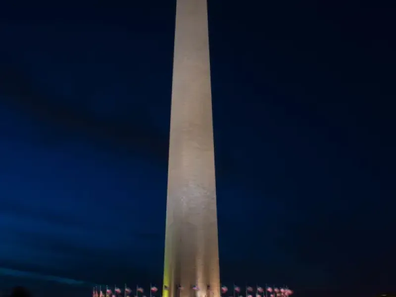 Washington DC Washington Monument illuminated at night surrounded by American flags under a deep blue sky