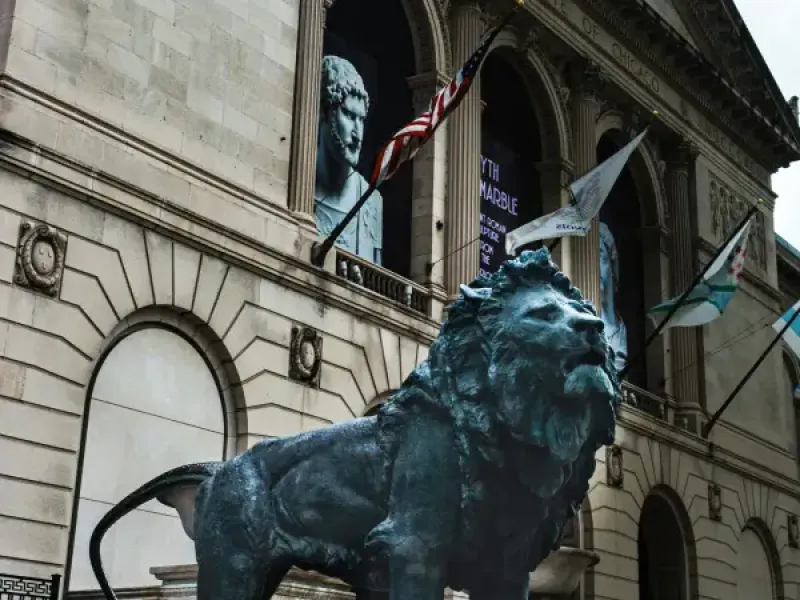 Bronze lion statue guards the entrance of the Art Institute of Chicago; with American and city flags visible behind it.