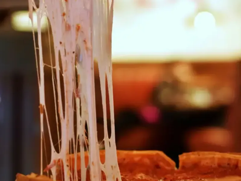 A slice of Chicago deep-dish pizza being lifted; stretching long strands of melted mozzarella from the pan below.