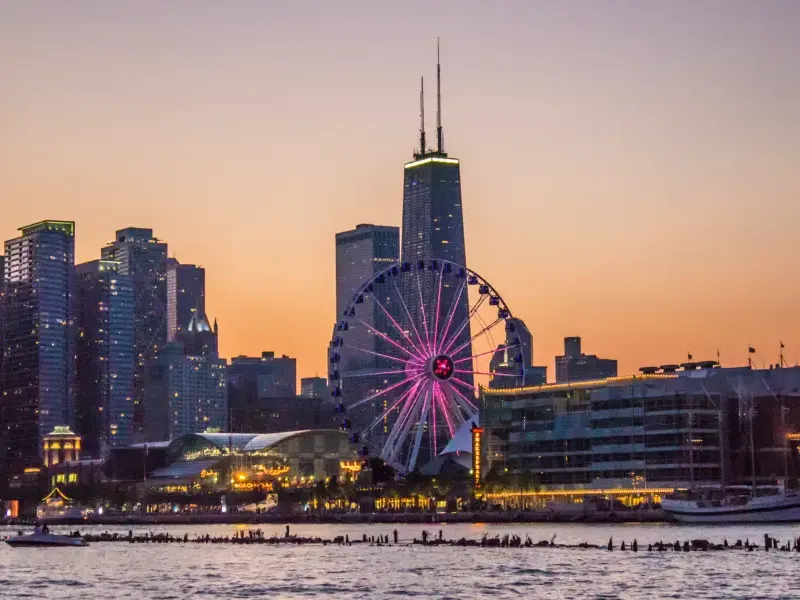 Chicago's Navy Pier Ferris wheel glowing pink at sunset with the John Hancock Center and city skyline behind; viewed from