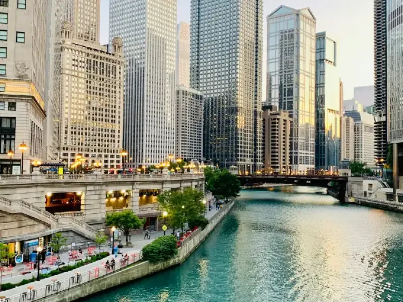 Chicago River Riverwalk with teal water; pedestrian promenade; and gleaming downtown skyscrapers at golden hour.