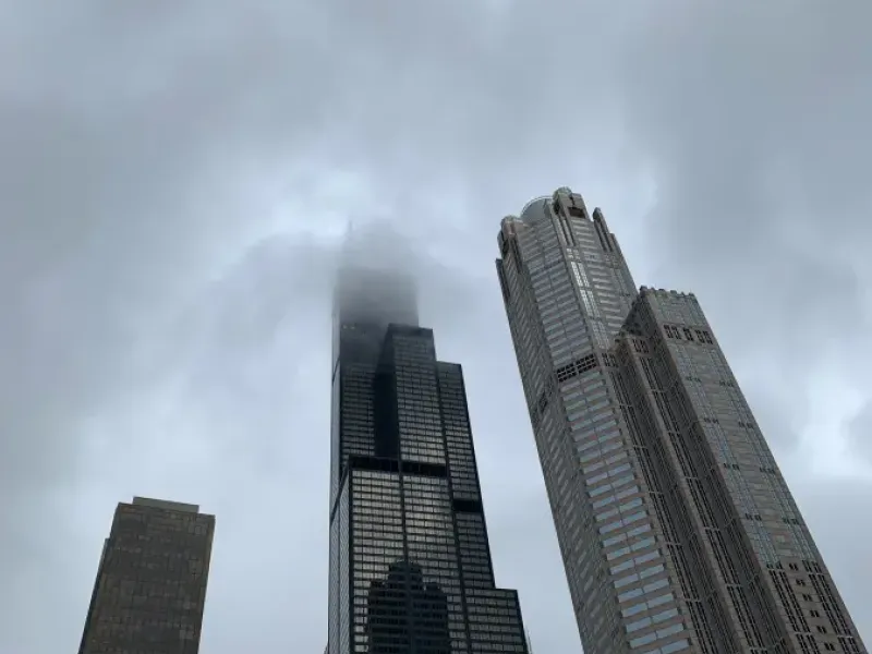 Willis Tower piercing low clouds on a stormy day in Chicago; viewed from street level alongside neighboring skyscrapers.