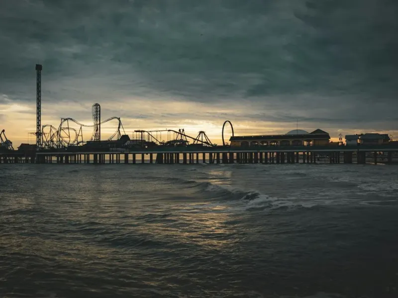 The Galveston Island Historic Pleasure Pier roller coaster silhouetted over the Gulf of Mexico at dusk.