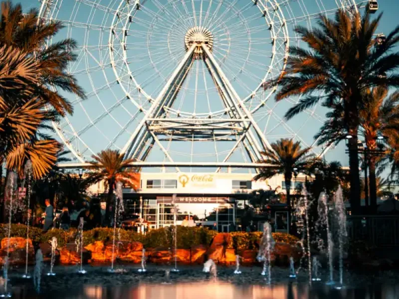 The ICON Park ferris wheel rises above palm trees and fountains at dusk in Orlando; FL.