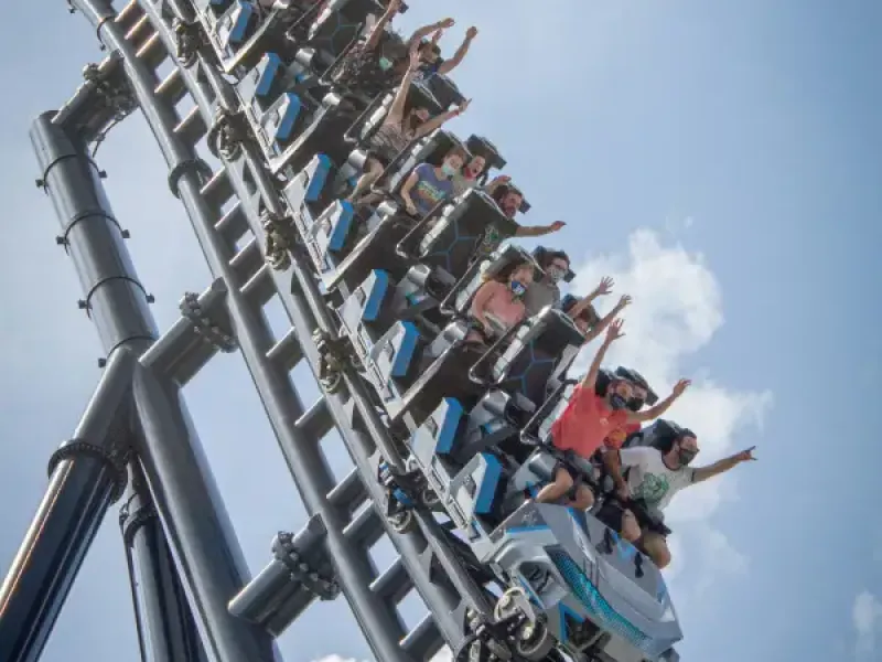 Riders with hands raised on a steep roller coaster climb at an Orlando; FL theme park on a partly cloudy day.