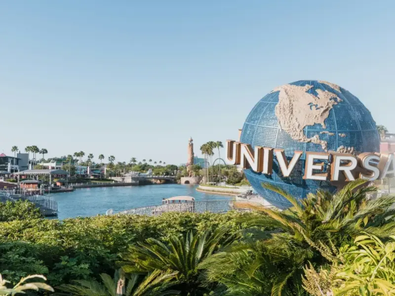 Universal Studios globe landmark beside a lagoon with palm trees and park buildings at Universal Orlando FL on a clear day.