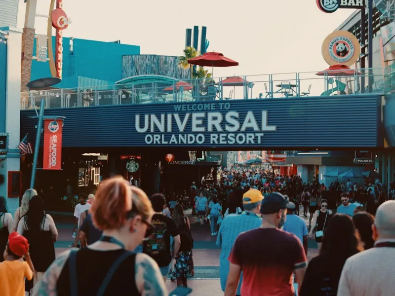 Crowds walk beneath the Welcome to Universal Orlando Resort sign in Orlando, Florida at dusk