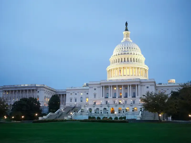 The illuminated U.S. Capitol Building in Washington; DC glows at dusk against a blue twilight sky with manicured grounds.