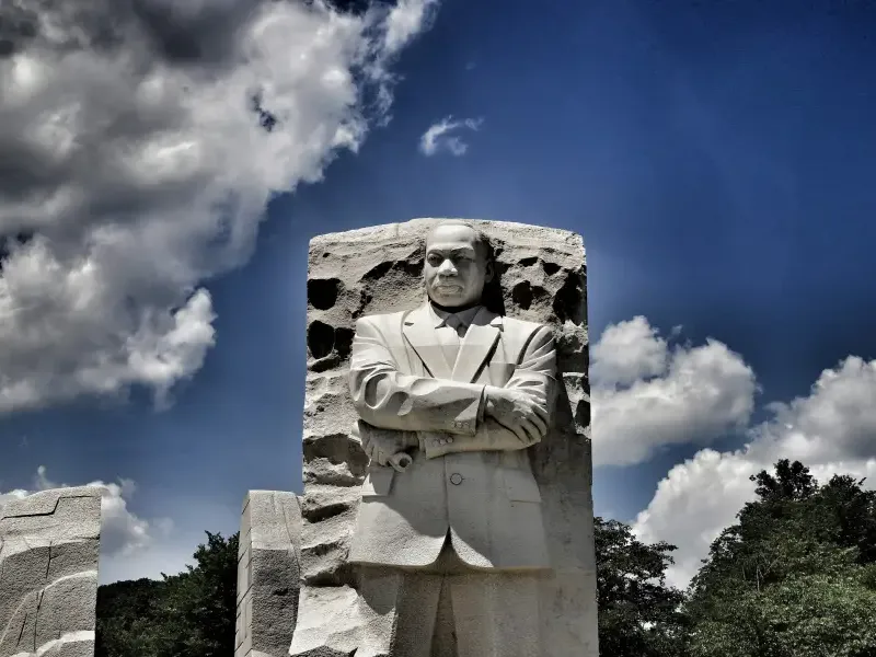 The Martin Luther King Jr. Memorial Stone of Hope sculpture in Washington DC; arms crossed; against a dramatic blue sky.