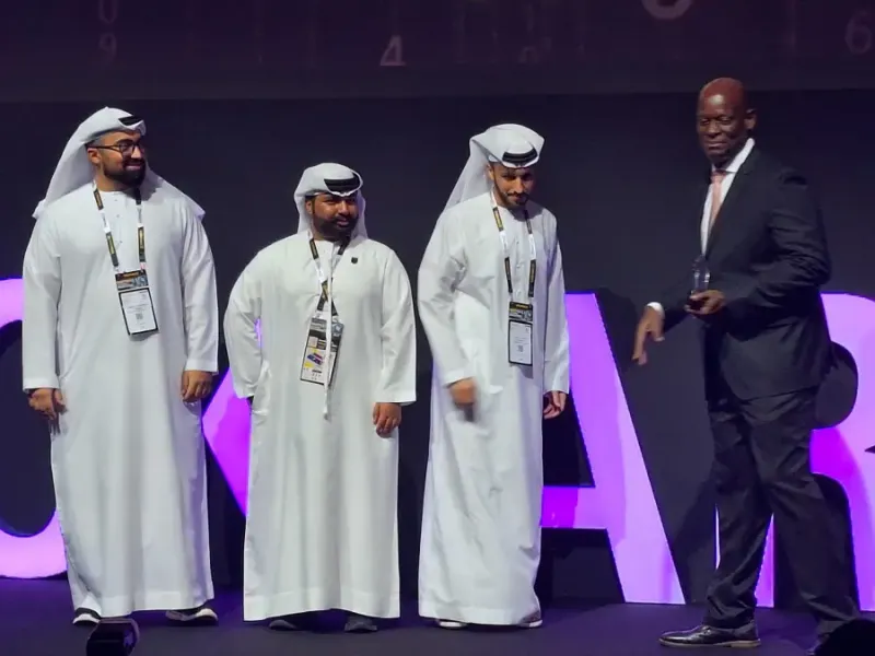 Three men in traditional Emirati dress receive an award on stage at Intersec from a man in a dark suit holding a trophy.