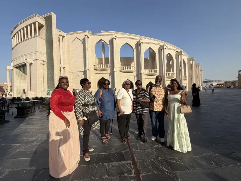 Seven travelers pose together at Katara Cultural Village in Doha Qatar; with the ornate amphitheater facade behind them.