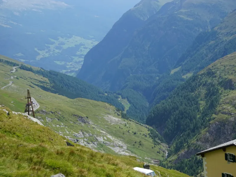 A broad Austrian alpine valley in late summer, green to the treeline with a farmhouse on the slope and bare rock above.