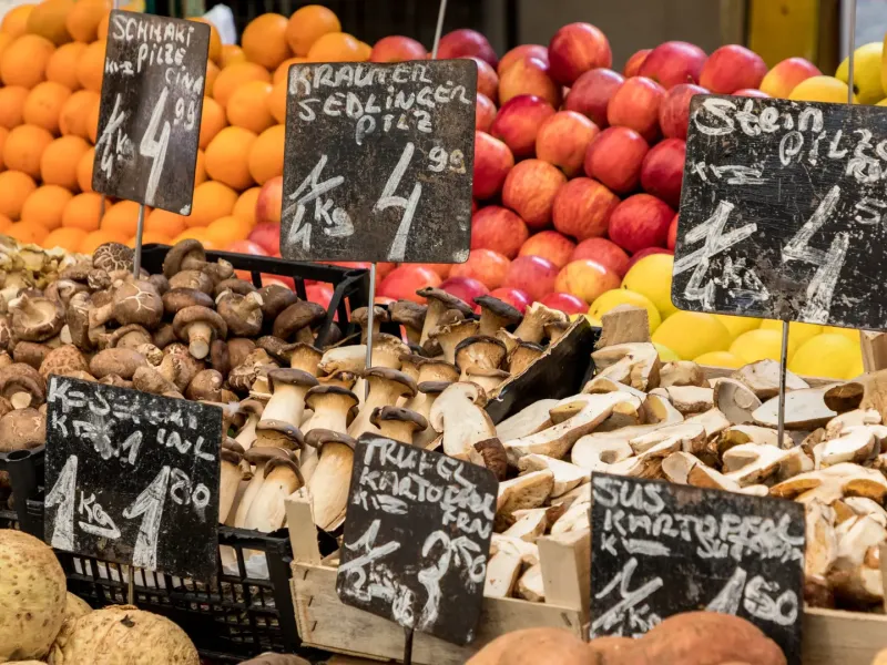 Mushrooms, oranges, apples and lemons banked up on a Naschmarkt stall in Vienna behind chalked price signs written in German.