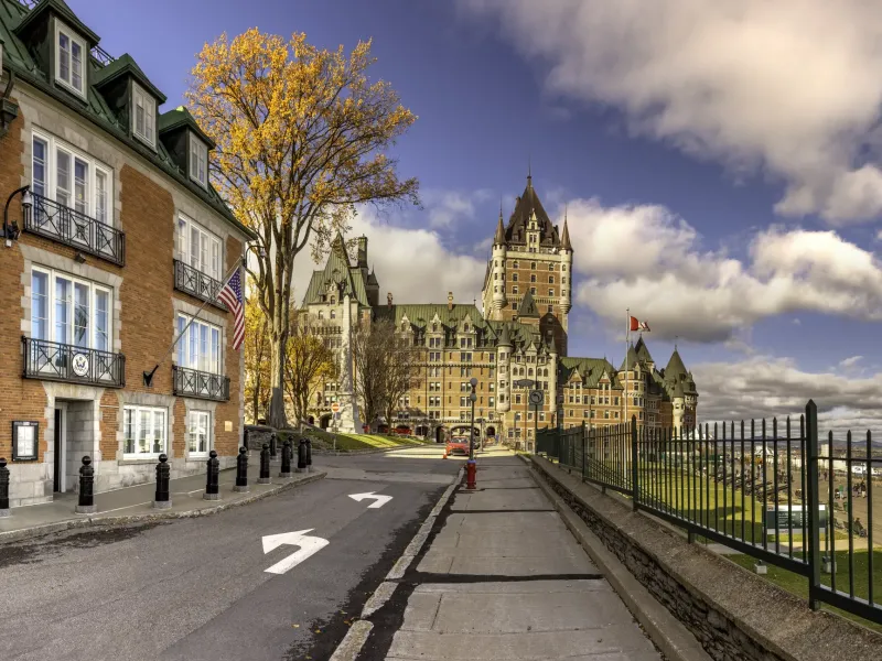 A turreted copper roofed hotel rising above a quiet street of brick and stone buildings, with an autumn maple in leaf.