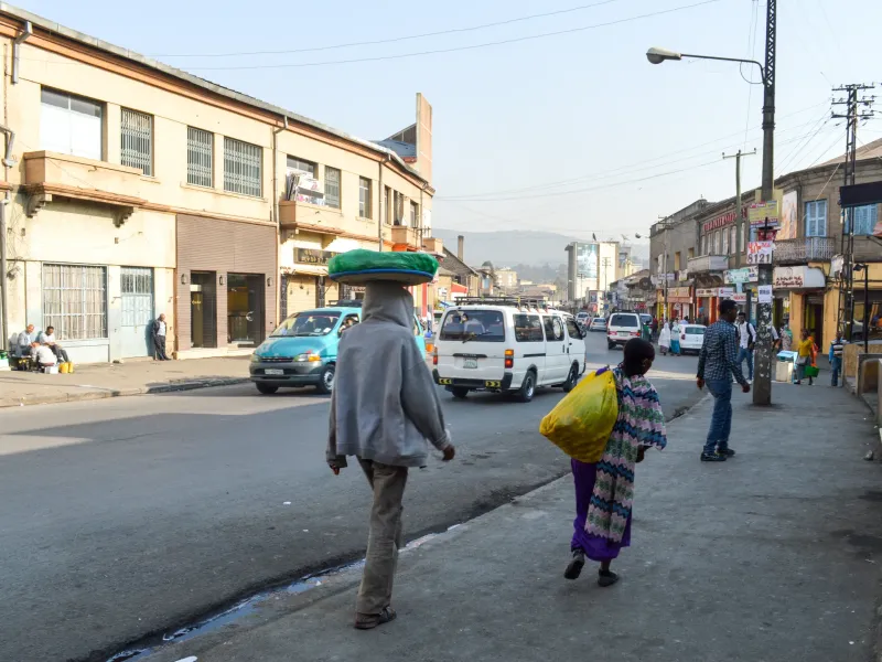 A street in central Addis Ababa, Ethiopia, lined with low shopfronts, minibuses at the curb and people on the roadside.