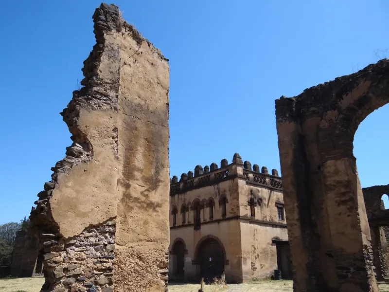 Standing stone walls and arches of the Royal Enclosure at Gondar, Ethiopia, framing a crenellated tower under a clear sky.