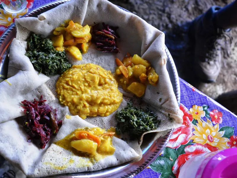 A shared platter of injera in Ethiopia topped with mounds of lentil, split pea and cooked green vegetable dishes.