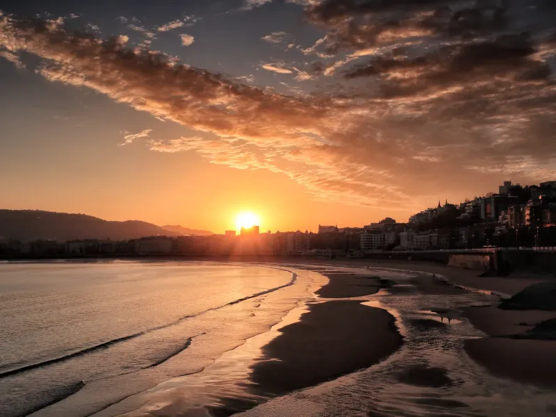 Low sun over La Concha bay at San Sebastian, Spain, the city curving around the shoreline behind the beach.