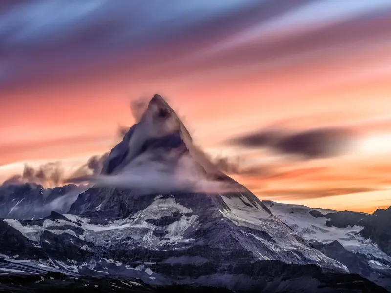 The pyramid peak of the Matterhorn in Switzerland at sunset, cloud streaming from its summit ridge